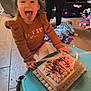 child, birthday_cake, candle, tongue_out, celebration, toy, blanket, floor, person, table, sweater, indoor, happy, smiling, party, young_child, playful, home, light, fun