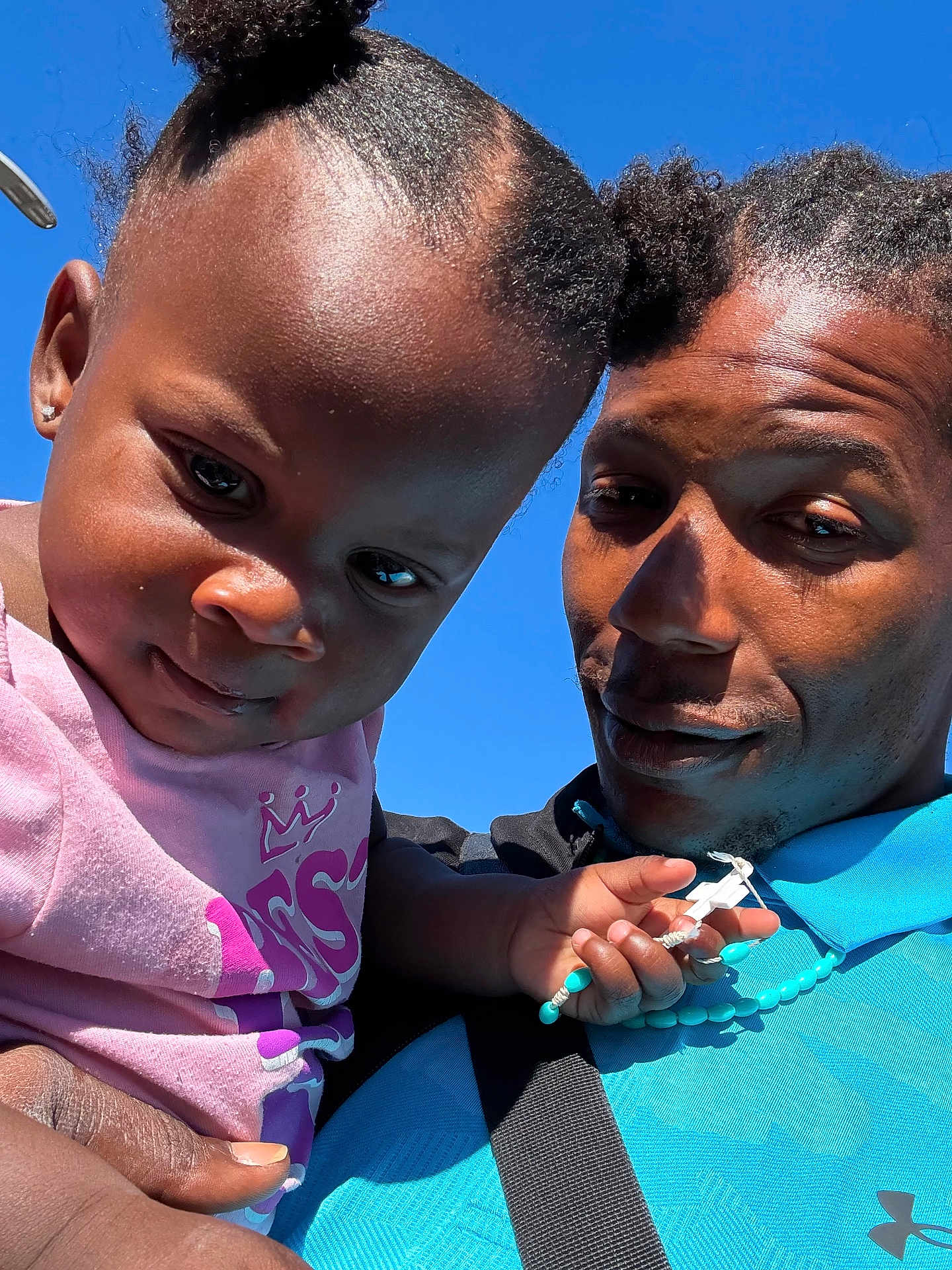 Zamoni is registered to the contest to win money with this photo: adult, beads, blue_shirt, blue_sky, casual_clothing, child, closeup, cross, curly_hair, hairstyle, happy, holding, necklace, outdoor, person, pink_shirt, portrait, selfie, smile, sunlight