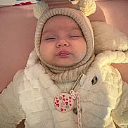 Arya participe au concours pour gagner de l'argent avec cette photo : baby, infant, child, coat, hat, pom_poms, knitwear, sleepy, face, pink_background, handprints, soft_texture, button, chain, warm_clothing, portrait, cute, indoors, smiling, person