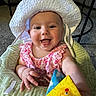 baby, child, smiling, hat, white_hat, pink_dress, indoor, toy, baby_seat, green_seat, happy, face, hand, carpet, table, person, infant, cute, colorful_toy, portrait