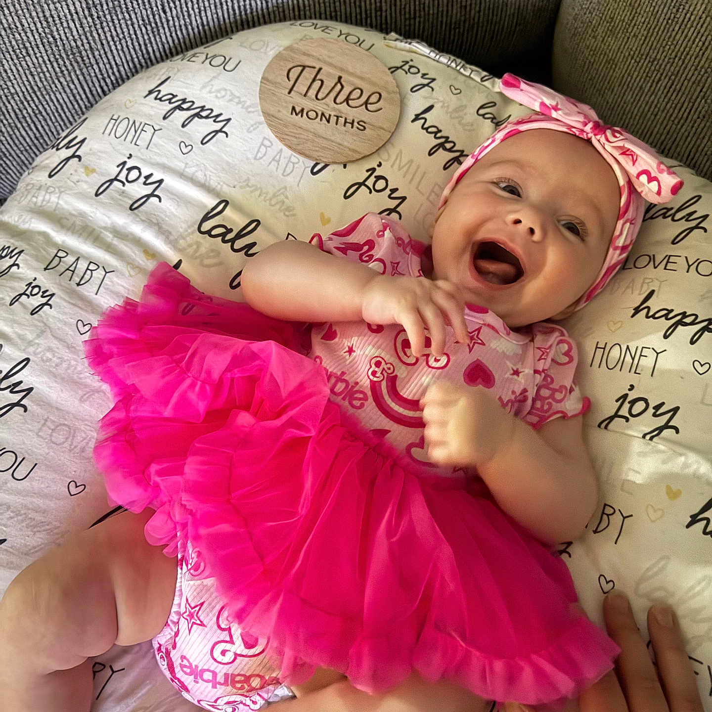 Charlotte is registered to the contest to win money with this photo: baby, infant, pink_tutu, headband, smiling, happy, three_months, pillow, patterned, lying_down, cute, child, apparel, hand, skin, face, indoors, soft_texture, joy, celebration