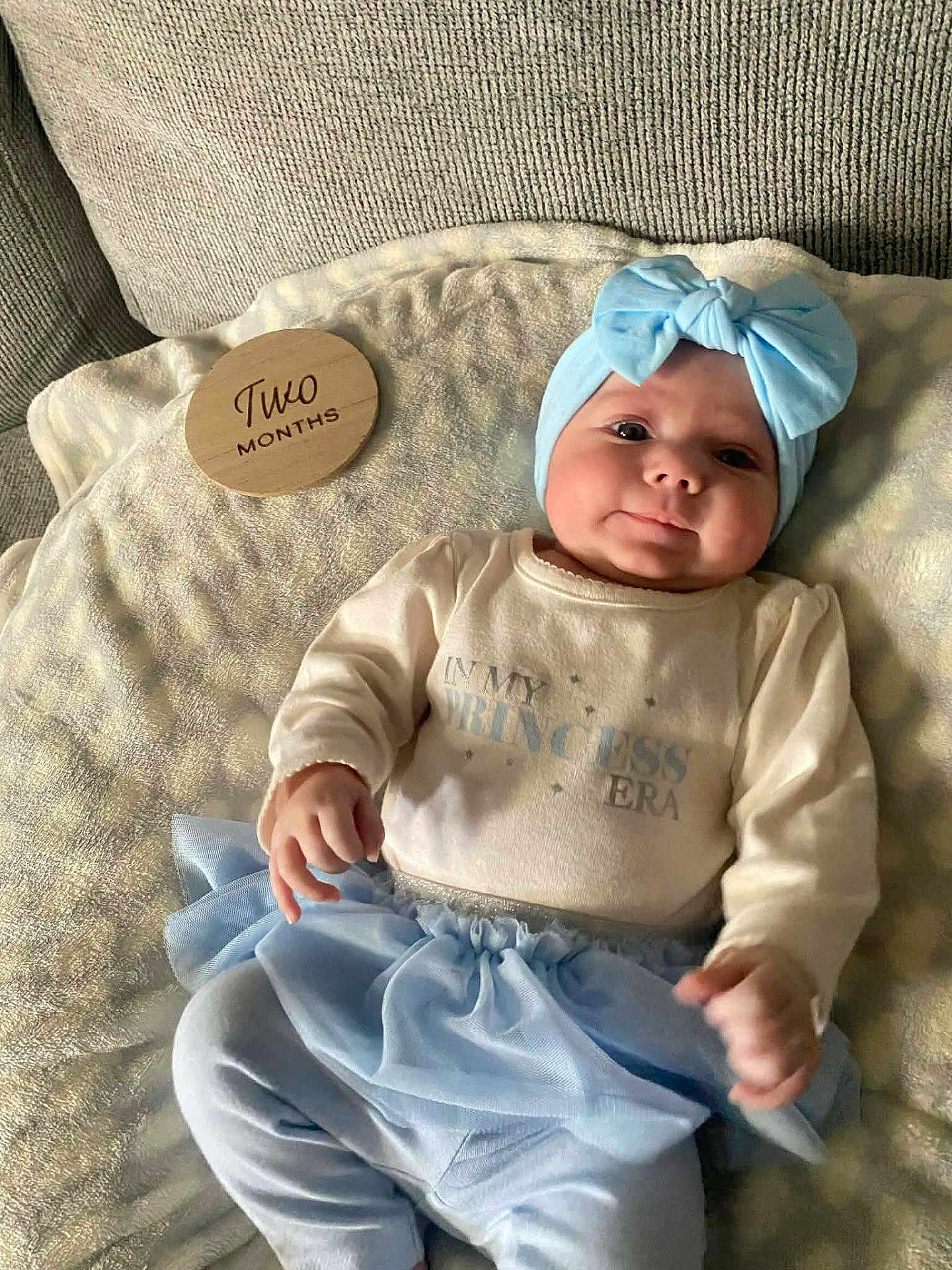 Charlotte joined the competition — help win amazing prizes! baby, infant, two_months, headband, bow, blanket, couch, onesie, tutu, skirt, hand, face, cheeks, eyes, portrait, indoors, soft_light, milestone_disk, cute, smiling