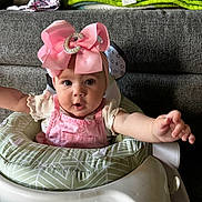 Charlotte is registered to the contest to win money with this photo: baby, infant, bow, pink, baby_walker, couch, blanket, indoor, child, cute, reaching, clothing, face, person, home, furniture, expression, headwear, sitting, curious