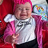 baby, child, smiling, happy, face, headband, flower, clothing, pink, jacket, tshirt, text, person, hand, tongue, adult, red, black_pants, indoor, portrait