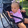 toddler, child, stroller, pink_bows, pink_outfit, sitting, outdoor, daylight, greenery, road, sidewalk, baby, cute, curious, person, young_child, summer, sunlight, safety_harness, park