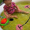 toddler, child, inflatable_pool, water, toy, pink_swimsuit, curly_hair, outdoor, grass, summer, playing, sitting, sunny, baby, water_play, recreation, fun, daylight, cute, kid