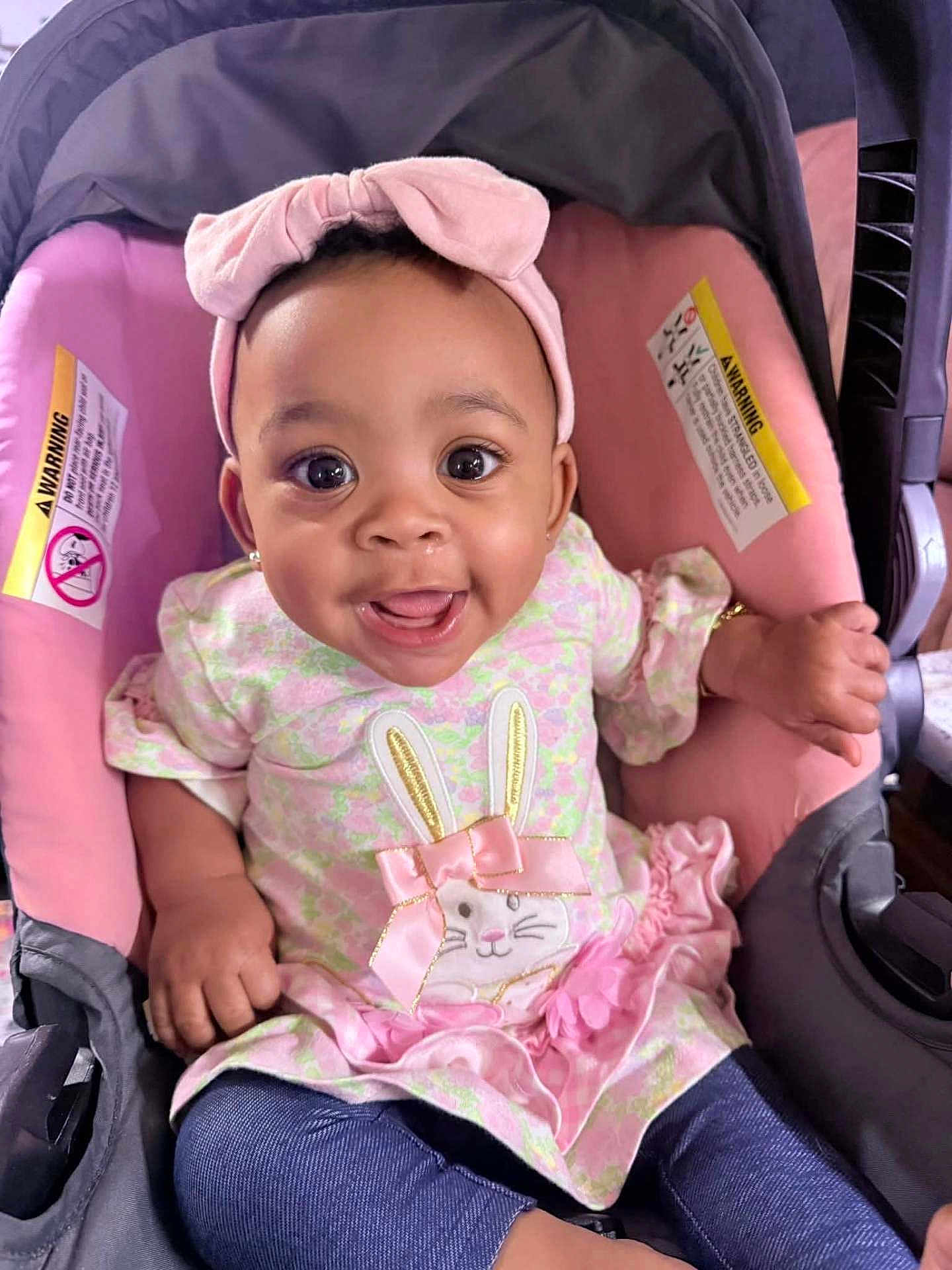 Arys is registered to the contest to win money with this photo: baby, child, infant, smiling, headband, pink, car_seat, cute, happy, dress, bunny, bow, clothing, portrait, toddler, sitting, face, person, indoors, accessory