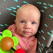Janelle participe au concours pour gagner de l'argent avec cette photo : baby, infant, blue_eyes, pink_shirt, toy, flower_toy, curious, child, face, closeup, cushion, pattern, fish_pattern, indoor, person, young_child, looking_at_camera, colorful, cute, portrait