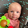 baby, infant, blue_eyes, pink_shirt, toy, flower_toy, curious, child, face, closeup, cushion, pattern, fish_pattern, indoor, person, young_child, looking_at_camera, colorful, cute, portrait