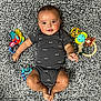 baby, infant, child, carpet, toy, onesie, smile, face, person, lying_down, play, cute, cheerful, colorful_toys, soft_texture, indoors, skin, hands, feet, expression