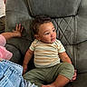 toddler, child, curly_hair, striped_shirt, green_pants, chair, upholstery, indoor, hand, skin, casual_clothing, sitting, cute, expression, person, plush_furniture, relaxed, young_child, comfort, family