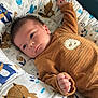 baby, infant, lying_down, cushion, animal_print, brown_clothing, sheep_patch, indoor, soft_lighting, cute, child, portrait, sleeping_bag, comfort, toddler, newborn, face, hand, blue, orange
