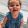 child, toddler, smiling, curly_hair, denim_dress, baby, portrait, indoor, sunlight, window, happy, face, cute, person, young_child, sitting, clothing, skin, hand, button