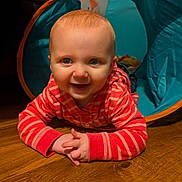 Evie is registered to the contest to win money with this photo: baby, child, smiling, crawling, play_tunnel, striped_clothing, hoodie, wooden_floor, indoor, happy, cute, person, face, blue, red, young_child, infant, hands, eyes, play