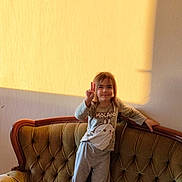 Vartic participe au concours pour gagner de l'argent avec cette photo : book, casual_clothing, child, cozy, cushion, girl, happy, home, indoor, jacket, long_hair, peace_sign, person, playful, smile, sofa, sunlight, tufted_sofa, vintage_furniture, wall