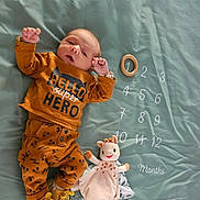 Léandro a rejoint le concours — aidez-le/la à gagner de superbes lots ! baby, infant, clothing, lying_down, milestone_blanket, months, toy, stuffed_animal, winnie_the_pooh, giraffe, footwear, cute, child, person, orange_clothing, text, number, smiling_toy, soft_toy, home