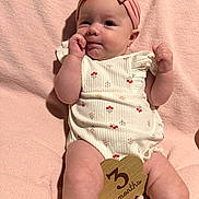 Marilyn is registered to the contest to win money with this photo: 3_months, adorable, baby, blanket, child, cute, fist, floral_romper, hand_near_mouth, headwear, indoors, infant, lying_down, pink_headband, portrait, skin, smiling, soft_texture, wooden_sign, young