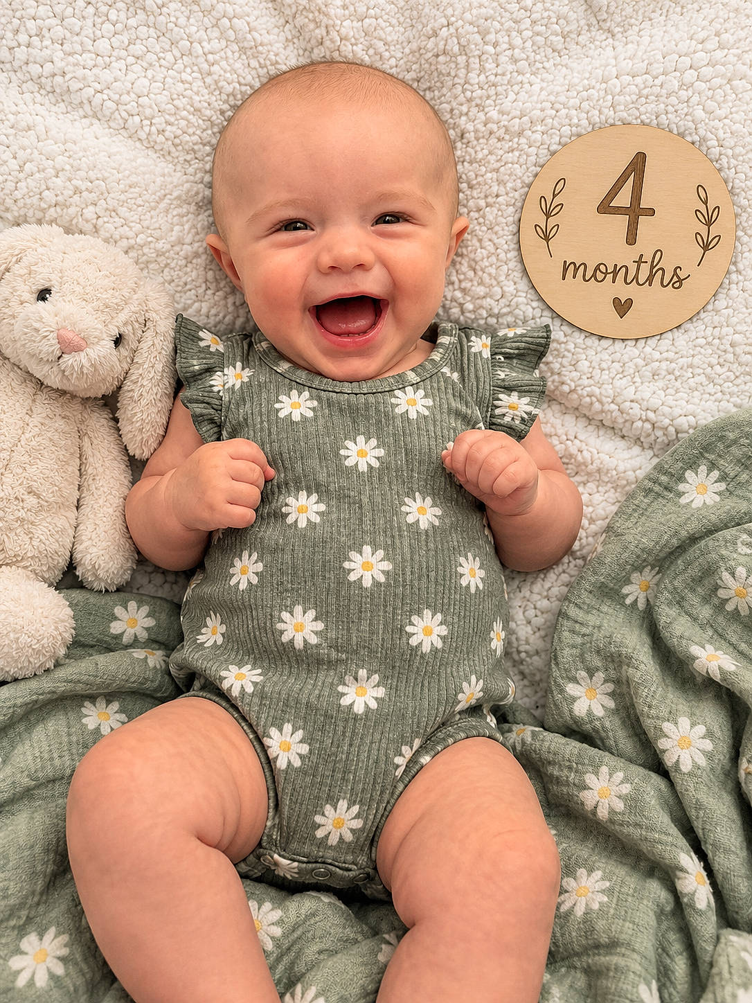Marilyn joined the competition — help win amazing prizes! baby, blanket, child, closeup, daisy, floral, four_months, green_clothing, happy, indoor, infant, laughing, lying_down, milestone, onesie, portrait, smiling, stuffed_animal, teddy_bear, wooden_sign