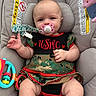 Marilyn is registered to the contest to win money with this photo: baby, infant, child, car_seat, pacifier, camouflage, military_style_clothing, portrait, sitting, indoor, toy, teether, safety_harness, car_seat_warning, gray upholstery, close_up, face, looking_at_camera, red_trim, photography