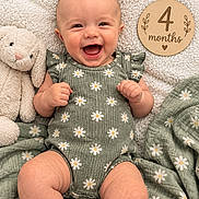 Marilyn joined the competition — help win amazing prizes! baby, infant, child, smiling, happy, portrait, indoor, lying_down, daisy_pattern, floral_clothing, green_outfit, blanket, stuffed_animal, rabbit, milestone_sign, four_months, wooden_sign, carpet, close_up, family_photo