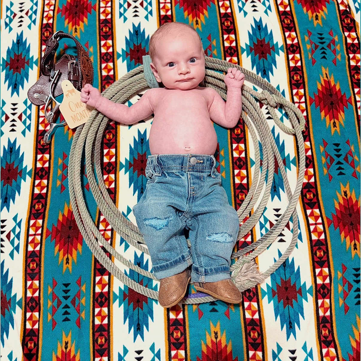 Kolter is registered to the contest to win money with this photo: baby, infant, denim_jeans, boots, rope, leather_accessory, patterned_blanket, colorful, one_month_tag, milestone, portrait, lying_down, cute, western_style, newborn, child, face, hands, feet, baby_clothing