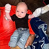 Kolter is registered to the contest to win money with this photo: baby, infant, mittens, jeans, black_shirt, brown_booties, adult_hand, red_shirt, leather_couch, blanket, blue_blanket, star_pattern, indoor, person, child, holding, casual_clothing, seated, cute, portrait