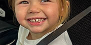 Reese is registered to the contest to win money with this photo: child, smiling, seatbelt, car_seat, vehicle, happy, young, girl, casual_clothing, short_sleeves, light_hair, indoors, portrait, closeup, safety, seat, car_interior, cute, teeth, joy