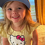 Reese joined the competition — help win amazing prizes! child, smiling, hat, baseball_cap, hello_kitty, shirt, yellow_shirt, pink_shorts, indoor, carpet, curtain, person, happy, face, long_hair, standing, cute, childhood, apparel, portrait