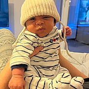 Lyam participe au concours pour gagner de l'argent avec cette photo : baby, child, infant, hat, knit_hat, striped_clothing, onesie, socks, indoor, person, cute, funny_face, hand, arm, furniture, window, television, blanket, cozy, expression