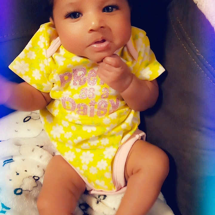 Lil Gbaby joined the competition — help win amazing prizes! baby, blanket, child, colorful_vignette, comfortable, cozy, cute, expression, face, hand, indoor, infant, legs, portrait, relaxed, seated, sheep_pattern, soft_lighting, yellow_onesie, young_child