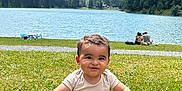 Zak participe au concours pour gagner de l'argent avec cette photo : baby, child, clouds, daytime, grass, greenery, happy, lake, landscape, mountains, nature, outdoor, person, scenic, sitting, sky, smiling, summer, sunlight, water
