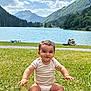baby, child, clouds, daytime, grass, greenery, happy, lake, landscape, mountains, nature, outdoor, person, scenic, sitting, sky, smiling, summer, sunlight, water