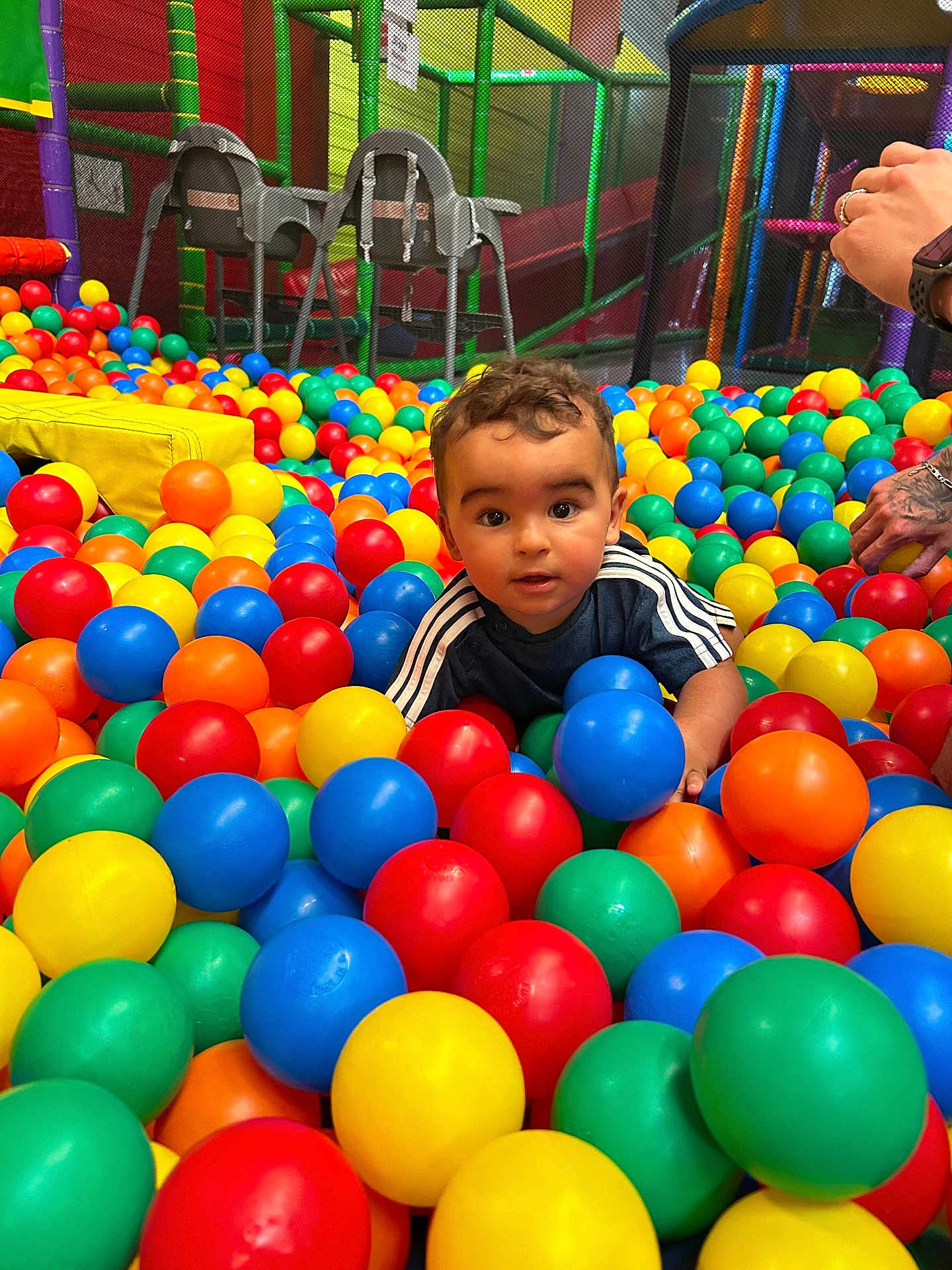 Zak a rejoint le concours — aidez-le/la à gagner de superbes lots ! ball_pit, blue_balls, blue_shirt, bright_colors, casual_clothing, child, colorful_balls, curly_hair, fun, green_balls, hands, indoor_playground, orange_balls, play_area, playtime, red_balls, smiling, toddler, toy, yellow_balls