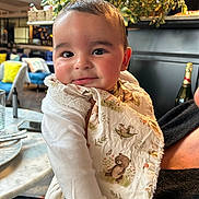 Zak participe au concours pour gagner de l'argent avec cette photo : baby, bib, chair, child, clothing, cushion, cute, expression, face, furniture, greenery, holding, indoor, infant, person, plant, portrait, smile, table, warm