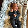baby, infant, smiling, black_onesie, bouncer, baby_bouncer, patterned_fabric, happy, indoor, wood_floor, child, cute, face, person, small_hands, head, joy, relaxed, seated, cozy