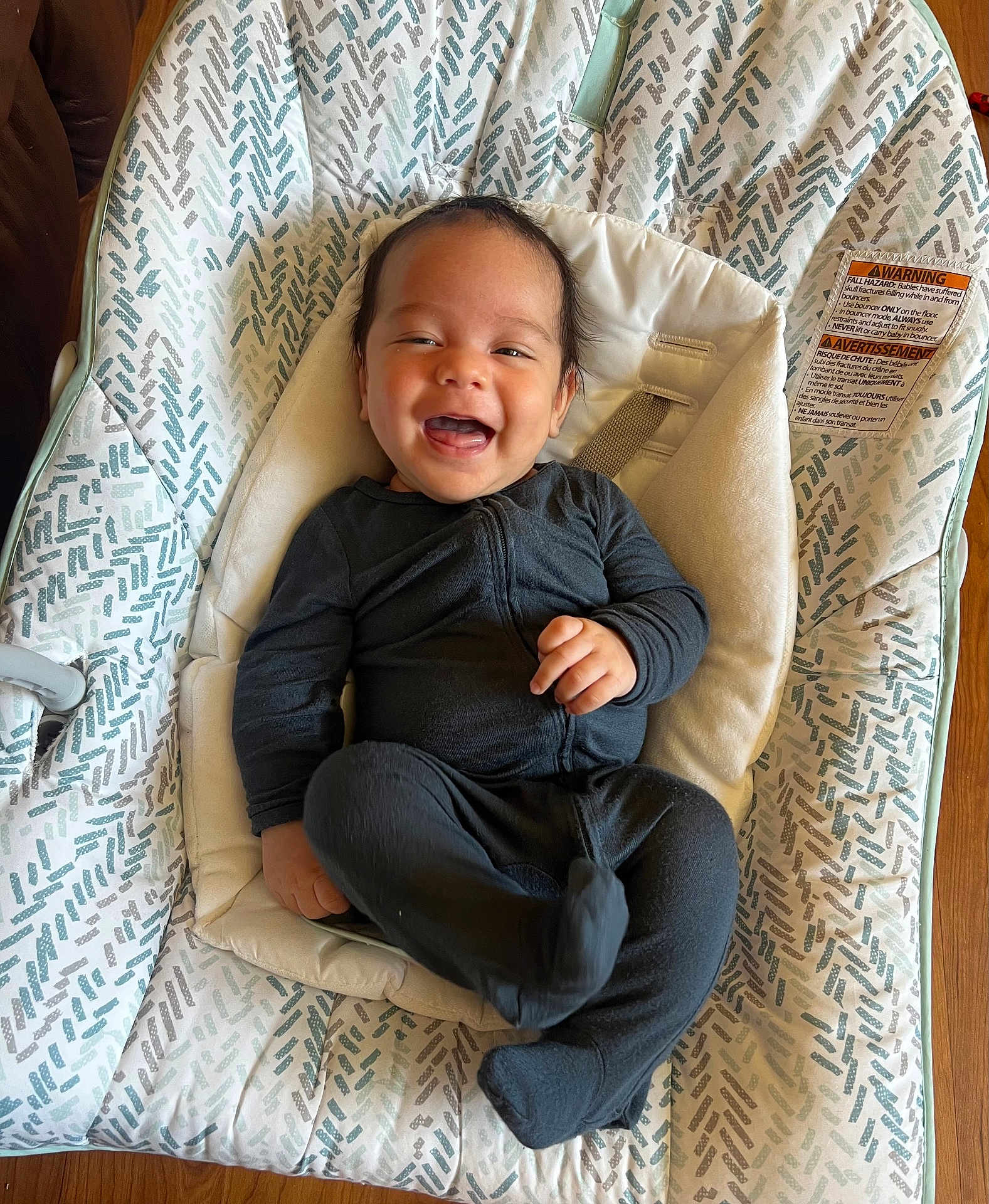 Samuel joined the competition — help win amazing prizes! baby, smiling, infant, black_clothing, baby_rocker, patterned_fabric, happy, indoor, wooden_floor, child, cute, face, person, one_person, infant_clothing, seat, relaxed, young_child, comfort, funny