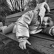 Emma Pauvret a rejoint le concours — aidez-le/la à gagner de superbes lots ! child, kid, bench, park, tree, puffer_jacket, coat, striped_tights, smile, playful, outdoor, winter, cold, wood_grain, monochrome, black_and_white, portrait, candid, legs, boots