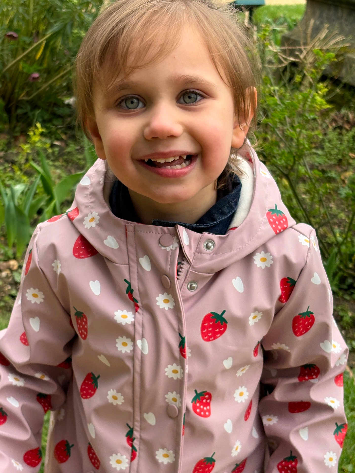 Emma Pauvret a rejoint le concours — aidez-le/la à gagner de superbes lots ! child, smiling, portrait, outdoor, garden, raincoat, strawberry_pattern, pink_jacket, hood, face, eyes, teeth, hair, happy, greenery, plants, grass, cute, clothing, ear