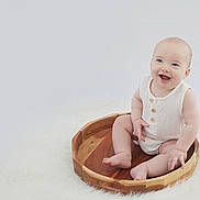 Leo joined the competition — help win amazing prizes! baby, child, smiling, wooden_tray, white_clothing, sitting, fluffy_surface, cute, happy, infant, portrait, indoor, soft_lighting, barefoot, round_tray, minimalist, light_background, cute_expression, small_hands, baby_skin