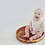 baby, child, smiling, wooden_tray, white_clothing, sitting, fluffy_surface, cute, happy, infant, portrait, indoor, soft_lighting, barefoot, round_tray, minimalist, light_background, cute_expression, small_hands, baby_skin