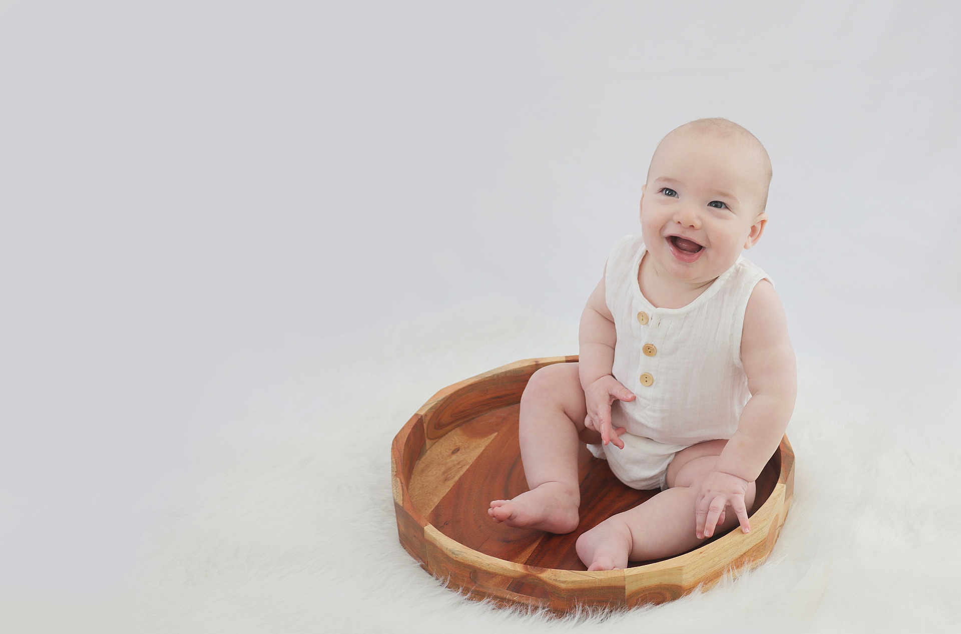 Leo joined the competition — help win amazing prizes! baby, child, smiling, wooden_tray, white_clothing, sitting, fluffy_surface, cute, happy, infant, portrait, indoor, soft_lighting, barefoot, round_tray, minimalist, light_background, cute_expression, small_hands, baby_skin