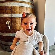 Louison participe au concours pour gagner de l'argent avec cette photo : toddler, child, smiling, happy, plush_toy, elephant_rocker, bow, hair_accessory, white_shirt, wooden_barrel, indoor, floor, tile_floor, furniture, cute, person, baby, playful, joyful, seat
