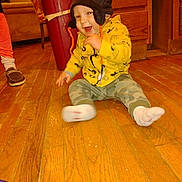 Steve is registered to the contest to win money with this photo: toddler, child, yellow_hoodie, hat, floor, wooden_floor, camo_pants, socks, smile, indoor, person, legs, shoes, moccasin, happy, motion_blur, wood_cabinet, furniture, warm_clothing, playful