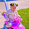 toddler, child, toy_car, pink, outdoor, sidewalk, grass, car, hair_clips, pigtails, sweatshirt, sandals, sunny, play, drive, handle, wheels, concrete, young_child, expression