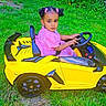 child, toddler, toy_car, yellow_car, grass, outdoor, girl, pink_dress, hair_bows, greenery, summer, play, vehicle, seat, steering_wheel, small_car, cute, portrait, nature, fun
