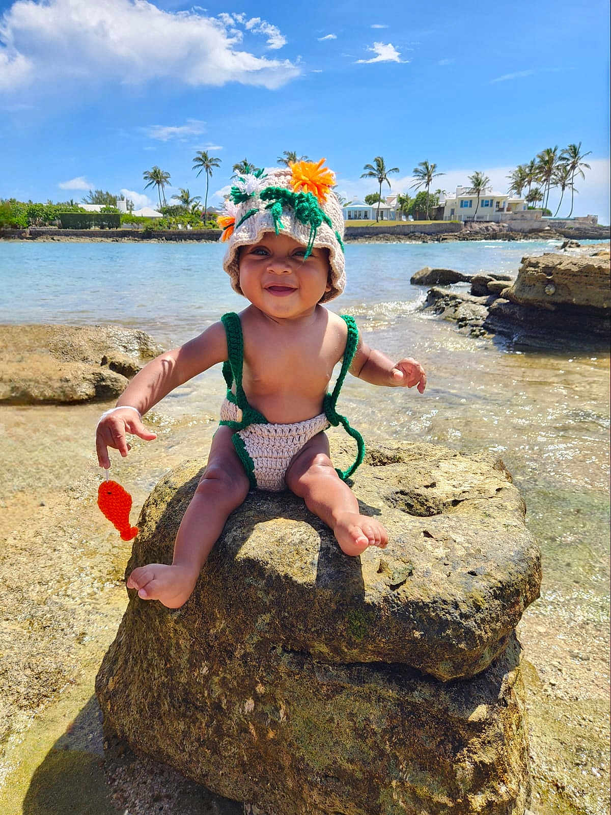 Tyme joined the competition — help win amazing prizes! baby, child, crocheted_hat, crocheted_outfit, rock, water, beach, ocean, tropical, palm_trees, sunny, smiling, toy, outdoor, nature, happy, barefoot, infant, blue_sky, vacation