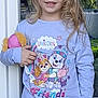 child, blue_eyes, blonde_hair, pajamas, plush_toy, smiling, standing, outdoor, door, glass, cartoon_characters, purple_clothing, long_hair, happy, toy, person, cute, young, daylight, casual