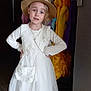 child, girl, dress, hat, indoor, posing, white_dress, cardigan, black_boots, floor, clothing_rack, colorful_clothes, hands_on_hips, portrait, fashion, young, person, floor_tiles, accessory, standing