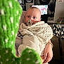 Wyatt joined the competition — help win amazing prizes! baby, pacifier, blanket, hand, person, indoor, cactus, blurred_object, wall_art, television, room, furniture, decor, blue_eyes, curious, wrapped, child, holding, cozy, portrait