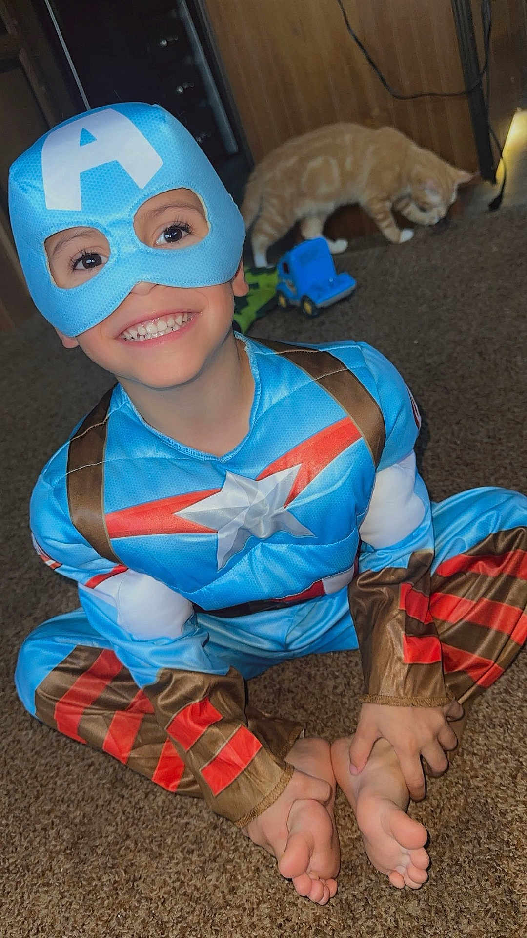 Ashtyn joined the competition — help win amazing prizes! barefoot, blue, brown, captain_america, carpet, cat, child, costume, cute, furniture, happy, indoor, mask, person, playful, red, room, sitting, smile, toy_truck